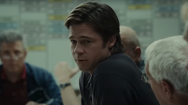 Brad Pitt as Billy Beane sits at a table surrounded by scouts in Moneyball