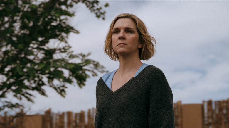 Rhea Seehorn as Carol Sturka standing in a backyard looking disheveled in Pluribus