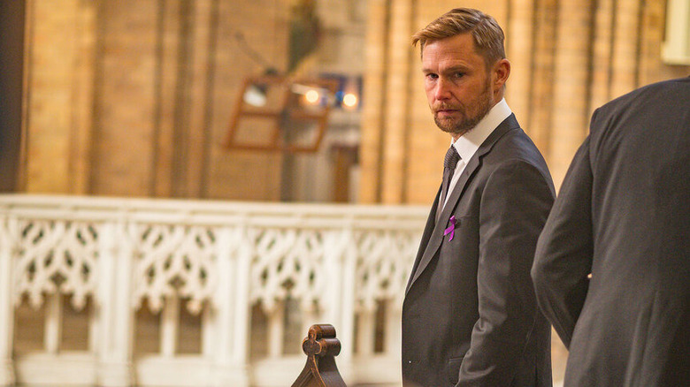 Brian Geraghty's Sean Roman stands in a church wearing a suit in Chicago P.D.