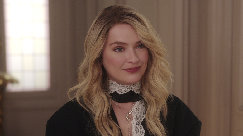 Camille smirking in a black top with white lace in Emily in Paris