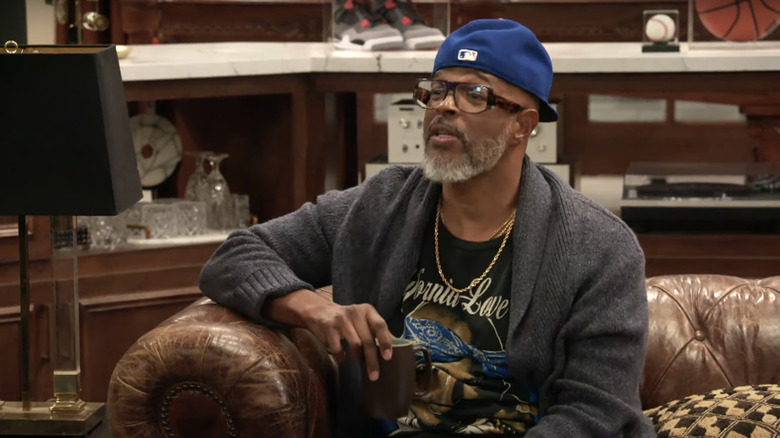 El Poppa de Daman Wayans se sienta en una silla hablando con alguien fuera de la pantalla en la casa de Poppa