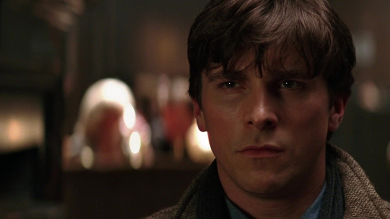 Bruce Wayne dari Christian Bale melihat ke seberang bingkai di Batman Begins