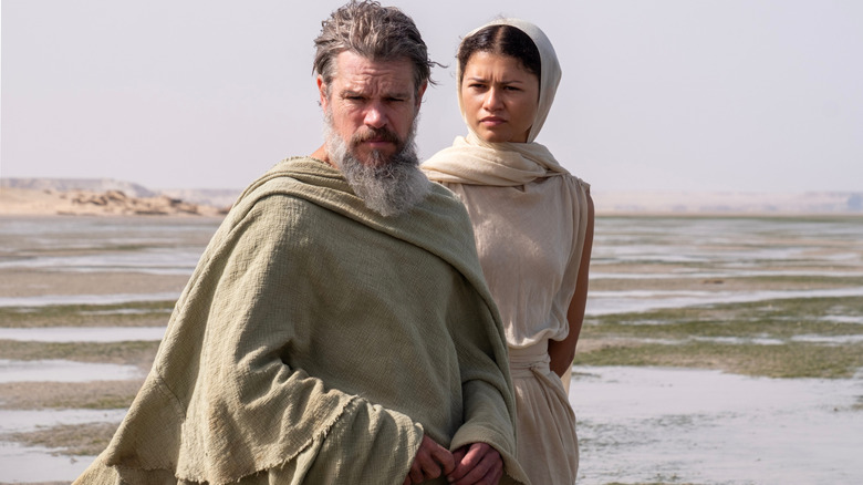 Matt Damon as Odysseus standing on a vast plain with Zendaya as Athena behind him in The Odyssey