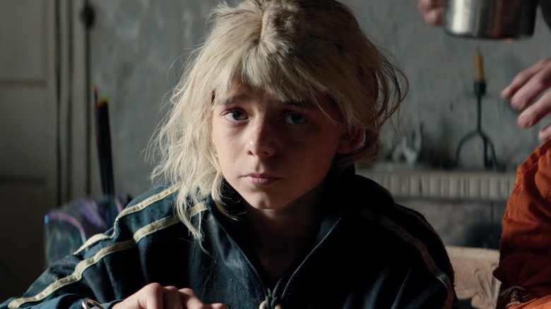Alfie Williams as Spike with his blonde wig sitting at a dining table in 28 Years Later: The Bone Temple