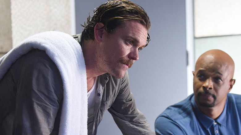 Martin Riggs leaning over with a towel on his shoulder while Roger Murtaugh looks on in Lethal Weapon