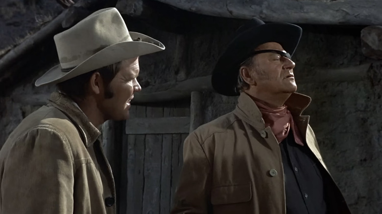 Glen Campbell's Ranger La Boeuf stares at John Wayne's Reuben J "Rooster" Cogburn  as he looks off into the distance in True Grit