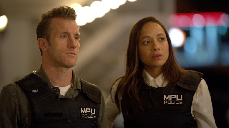 Scott Caan as Jason Grant standing next to Dania Ramirez as Nikki Batista in their police vests in Alert: Missing Persons Unit