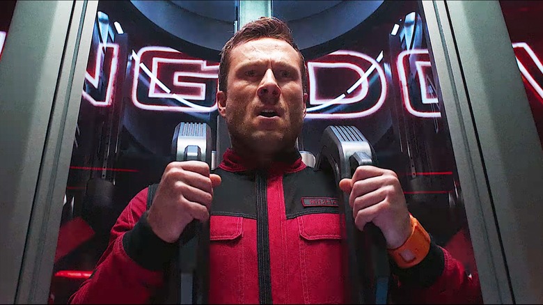 Glen Powell's Ben Richards holding on to a metal harness in The Running Man