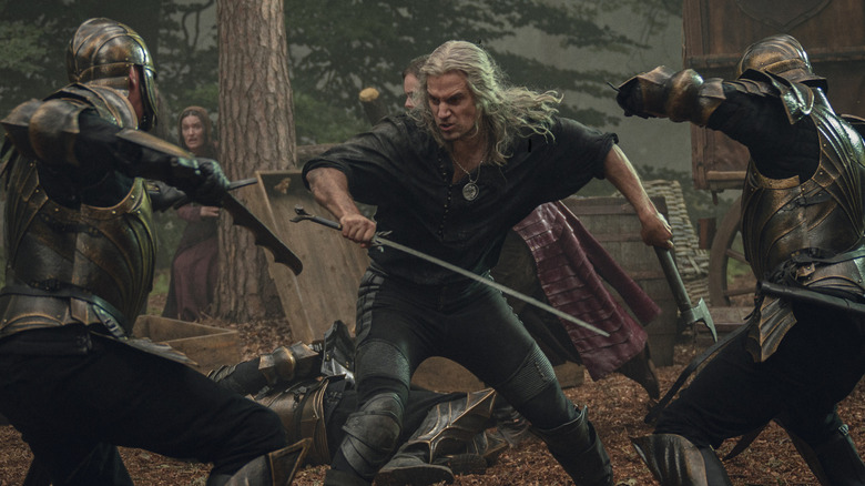 Henry Cavill as Geralt of Rivia fighting off several enemies with a sword and axe in The Witcher