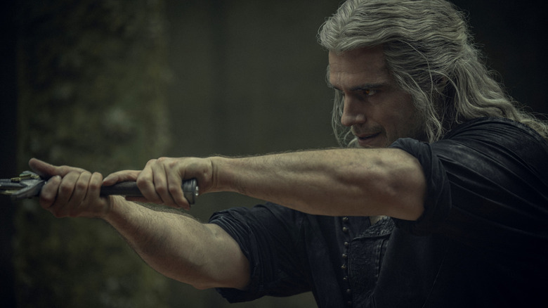 Henry Cavill as Geralt of Rivia wielding a sword in a fighting stance in The Witcher
