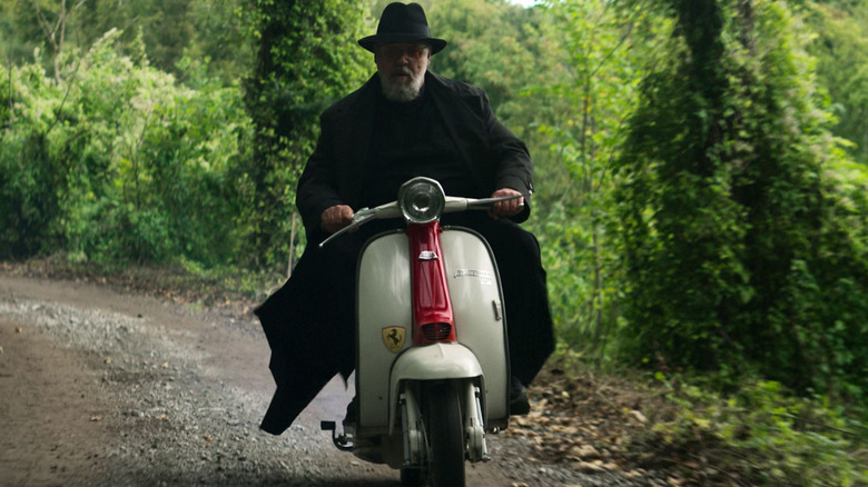 Father Gabriele Amorth (Russell Crowe) rides his vespa through a forest in The Pope's Exorcist (2023)