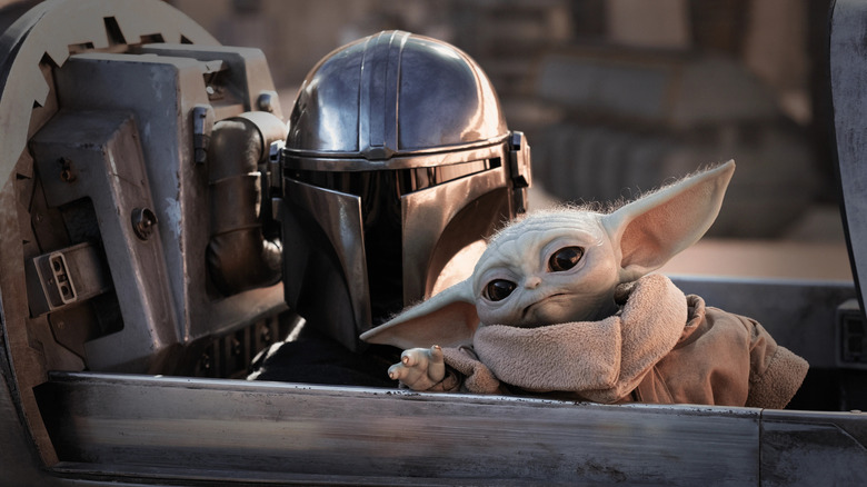 Din Djarin and GROGU sit in the cockpit from their spacecraft in the Mandalian 3 season