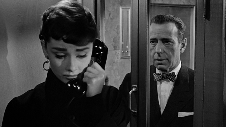 Audrey Hepburn's Sabrina Fairchild looks sad on the phone while Humphrey Bogarty's Linus Larrabee watches from outside the booth in Sabrina