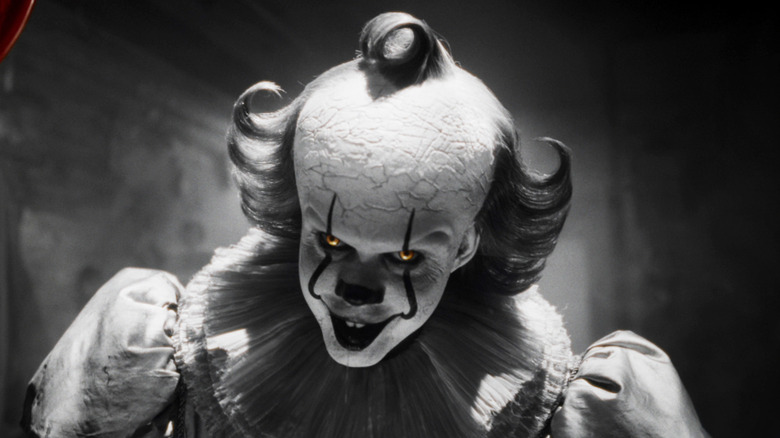 Bill Skarsgård's Pennywise stands in a corridor with his eyes glowing in It Welcome to Derry