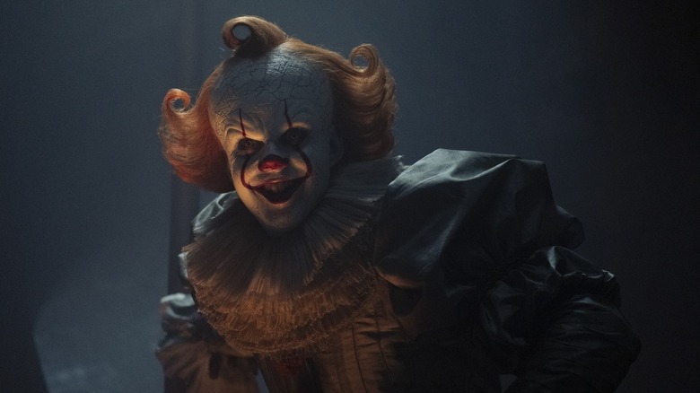 A smiling Pennywise standing in the shadows on IT: Welcome to Derry