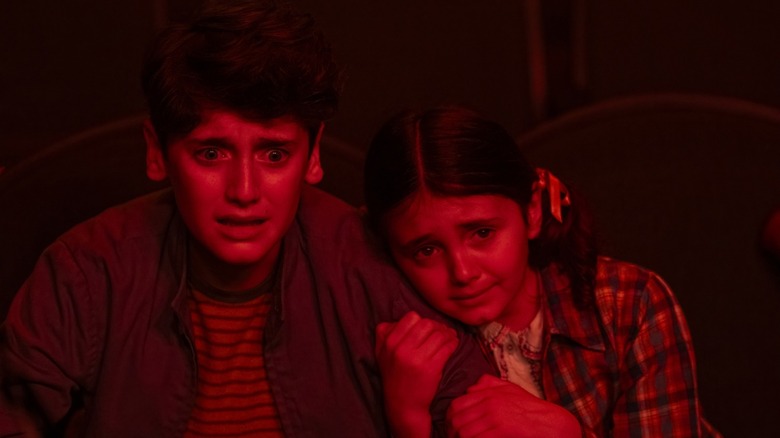 Jack Molloy Legault's Phil Malkin and Matilda Legault's Susie Malkin cower while illuminated in red light in It Welcome to Derry