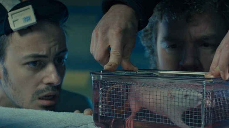 டோட் கிராஃப் ஹிப்பியாகவும், லியோ பர்மெஸ்டர் கேட்ஃபிஷாகவும் தி அபிஸில் ஒரு கூண்டில் திரவத்தை சுவாசிக்கும் எலியைப் பார்க்கிறார்கள்