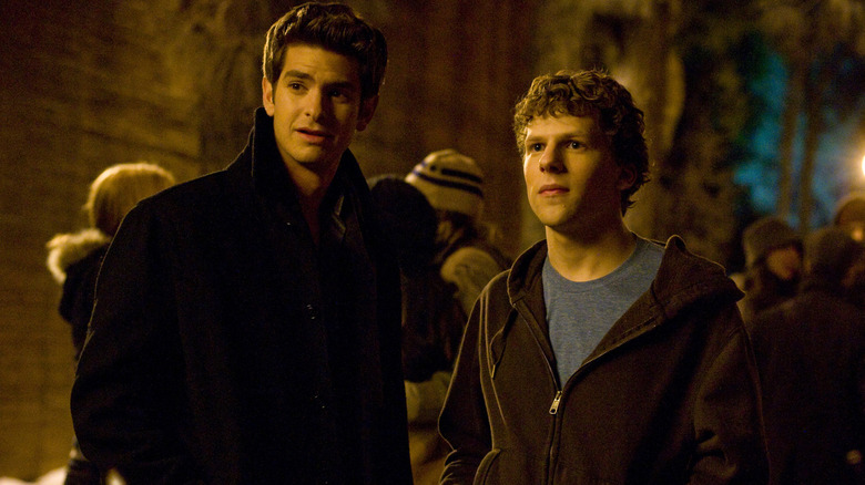 Jesse Eisenberg as Mark Zuckerberg and Andrew Garfield as Eduardo Saverin standing outside surrounded by people in The Social Network