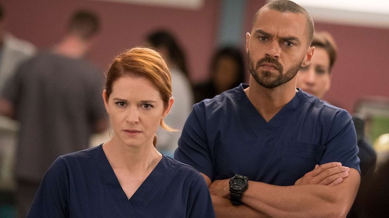 Jackson standing with his arms crossed behind April in the hospital lobby on Grey's Anatomy
