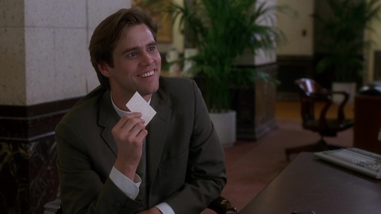 Jim Carrey's Stanley Ipkiss smiles as he sits in a bank in The Mask