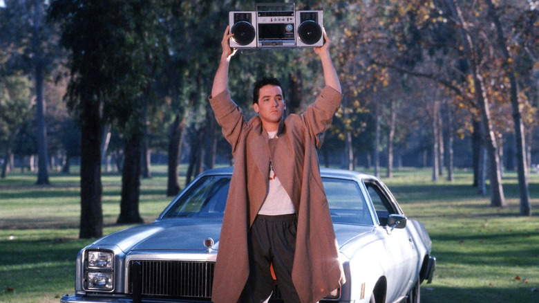Lloyd Dibler holding a bookbox over his head in front of a car in Say Anything...