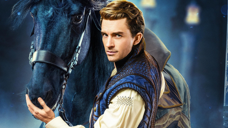 Jonathan Bailey's Fiyero fixes the cuffs on his shirt while standing in the woods in Wicked