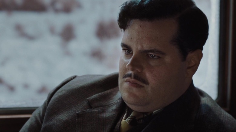 Josh Gad como Hector MacQueen sentado em pedra de assassinato no Orient Express