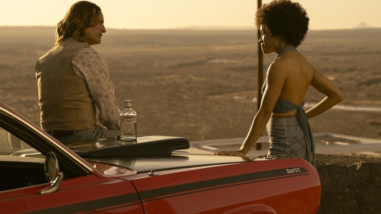 Josh Holloway as Jim Ellis sitting on the hood of his red Duster while Rachel Hilson as Nina Hayes stands nearby in the season finale of Duster