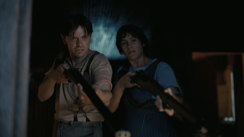 Peter Dreimanis as Bert and Lola Kirke as Joan stand side by side holding shotguns in Sinners