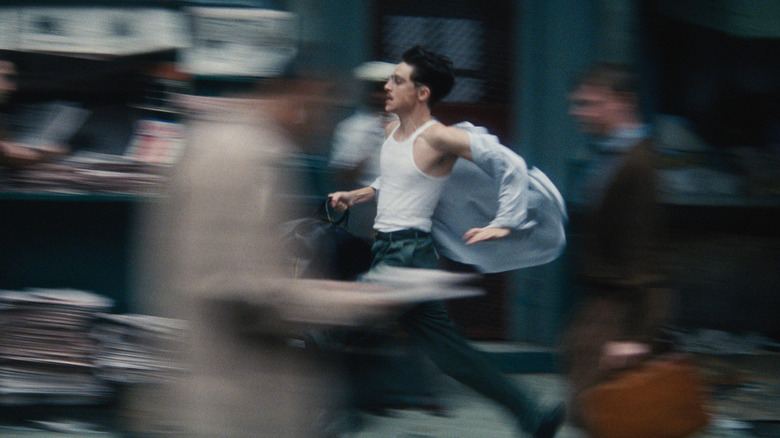 Timothée Chalamet as Marty Mouser running through the streets of New York City while holding a duffle bag in Marty Supreme
