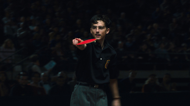 Timothée Chalamet as Marty Mouser holding a table tennis paddle and pointing in Marty Supreme