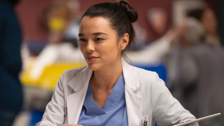 Mika in her white coat and scrubs looking at someone on Grey's Anatomy