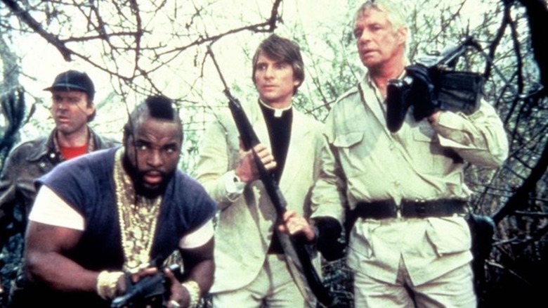 Dwight Schultz as Howling Mad Murdock, Mr. T as B.A. Baracus, Dirk Benedict as Faceman and George Peppard as Hannibal Smith hunker down in a forest in The A-Team