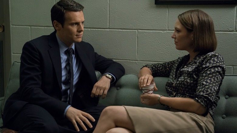 Jonathan Groff's Holden Ford sits on a couch with Anna Torv's Wendy Carr in Mindhunter