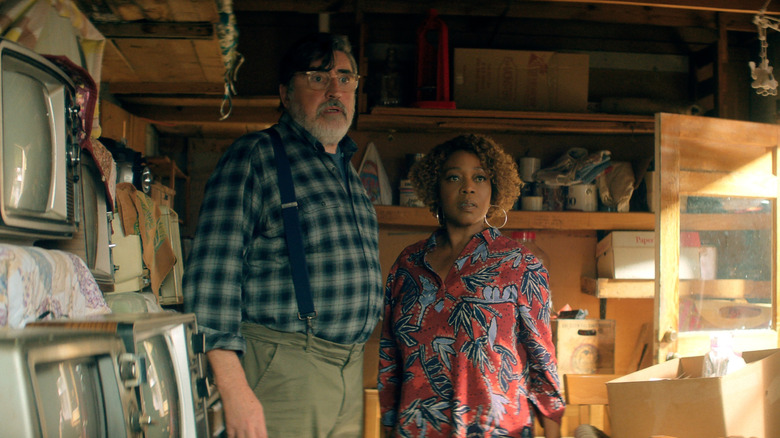 Alfred Molina as Sam standing in a cluttered garage next to Alfre Woodard as Judy in The Boroughs