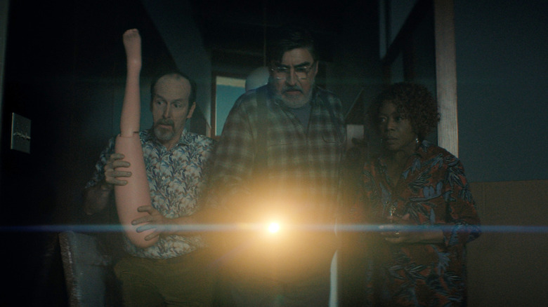 Denis O'Hare as Wally holding up a plastic leg as a weapon in a dark hallway next to Alfred Molina as Sam and Alfre Woodard as Judy in The Boroughs