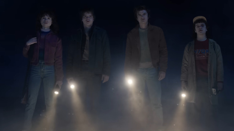 Nancy Wheeler, Jonathan Byers, Steve Harrington and Dustin Henderson standing in the dark with flashlights in Stranger Things 5