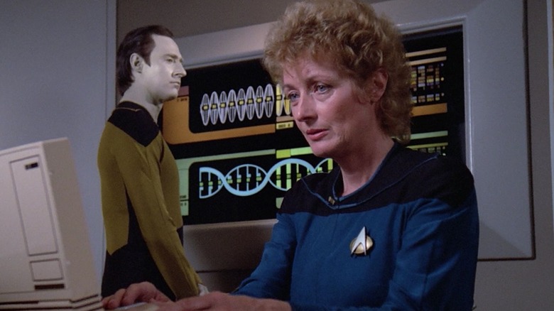 Dr. Pulaski at a desk with Data, offended, behind her