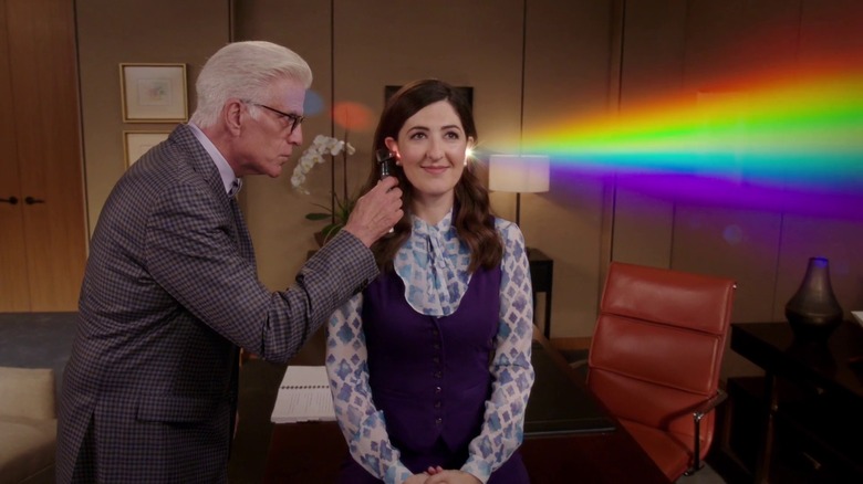 Ted Danson's Michael looks in the ear of D'Arcy Carden's Janet, which reflects a rainbow prism out the other side of her head, in The Good Place