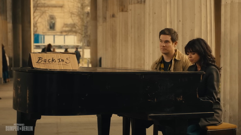 Adam Devine como Bumper y Sarah Hyland como Heidi sentada al piano en Pitch Perfect: Bumper en Berlín