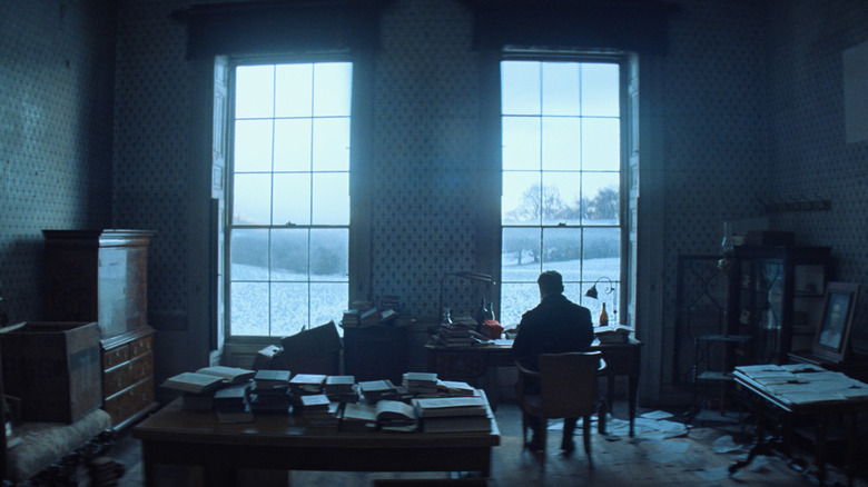 Cillian Murphy as Tommy Shelby sitting at a small desk in a large room in Peaky Blinders: The Immortal Man