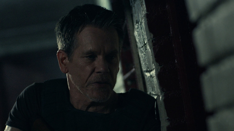 Kevin Bacon as Hub Halloran standing against a wall at night in The Bondsman