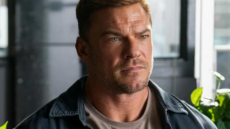 Alan Ritchson's Jack Reacher is seen in closeup while standing in a mall area in Reacher