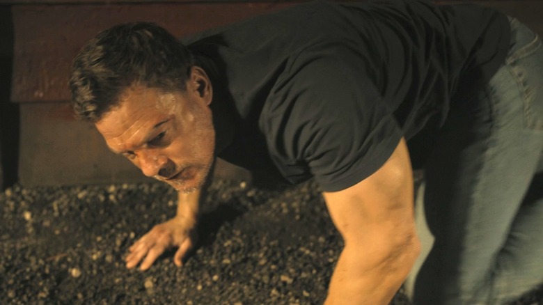 Alan Ritchson's Jack Reacher is seen on all fours looking shaken in Reacher
