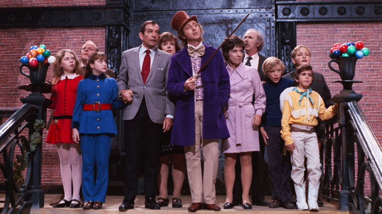 Willy Wonka, cercado por crianças e seus pais, gesticulando com uma bengala, uma cena de Willy Wonka e a fábrica de chocolate.