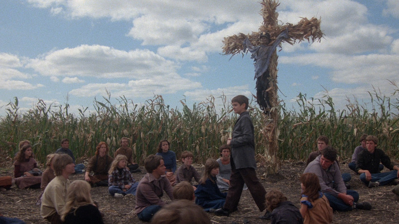Isaac walking among his disciples in a corn field, a corn cross with a skeleton on it in the background, from Children of the Corn