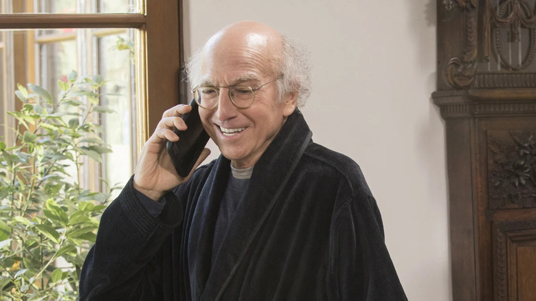 Larry David smiles while he is on the phone to curb your enthusiasm