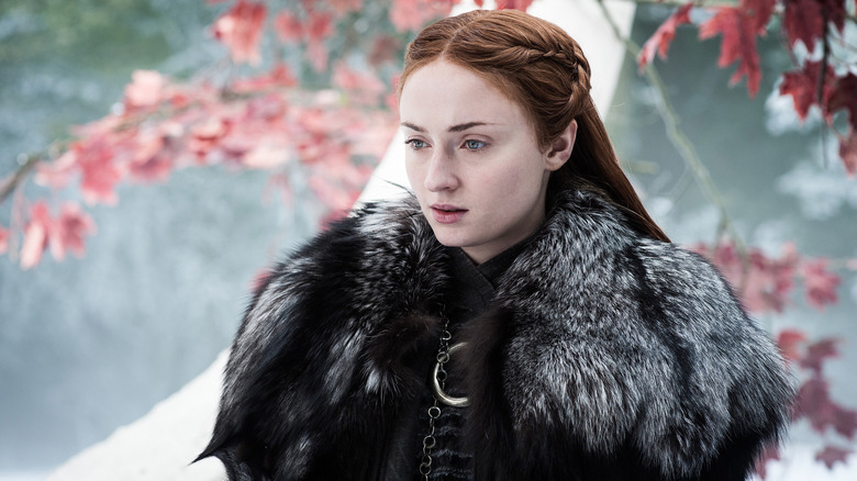 Sansa Stark (Sophie Turner) stands in front of a tree with red leaves in "Game of Thrones"