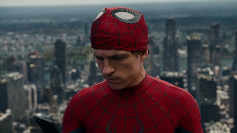 Tom Holland as Spider-Man with his mask up looking at his phone in Spider-Man: No Way Home