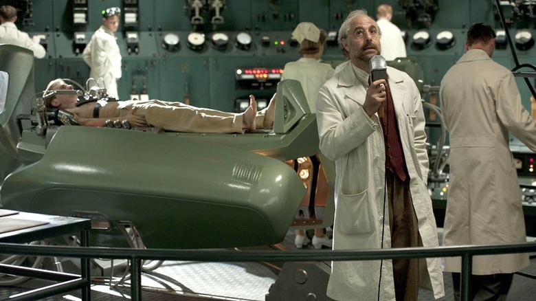 Dr. Erskine no meio de um laboratório de alta tecnologia, cercado por técnicos. Um Capitão América pré-transformação está em uma maca atrás dele.